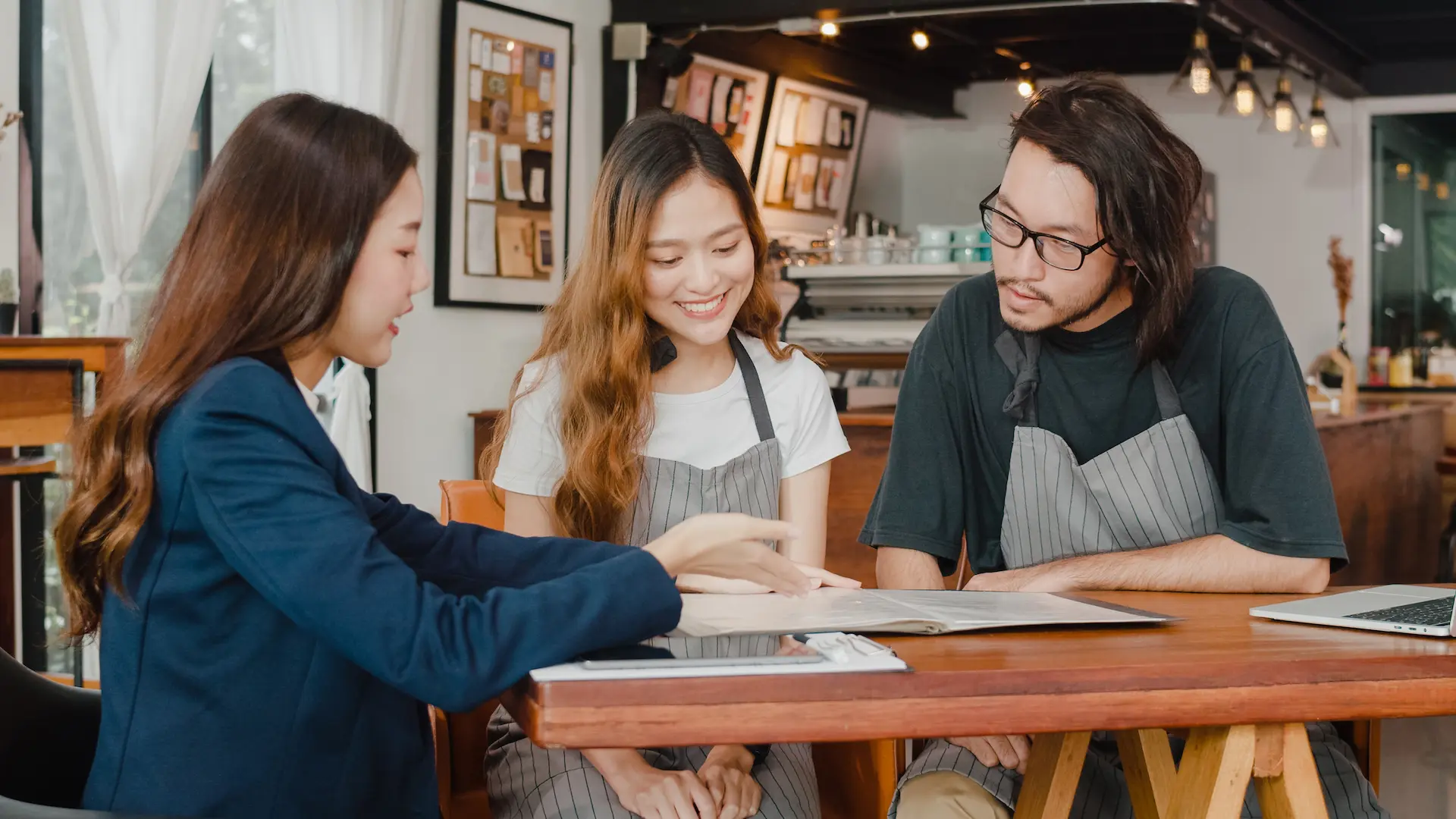 Cheerful small business owners couple meeting with consultant talking about business plan and finance in cafe. Young agent showing them documents.